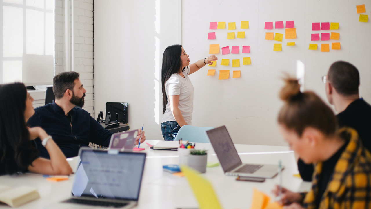Business woman collecting and visualizing ideas using colorful sticky notes on a wall in a conference.